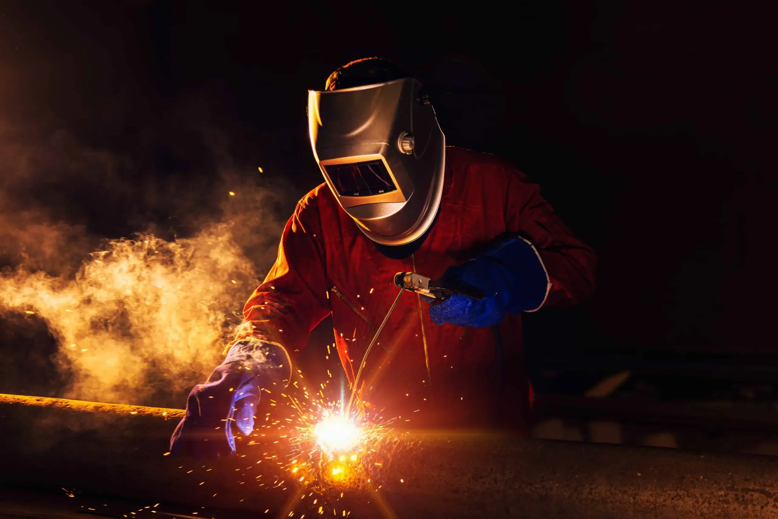 Man in full protective gear welding some metal in the dark.